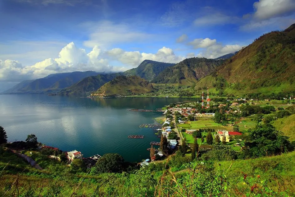 paket wisata danau toba: Panorama indah Danau Toba dengan perkampungan di tepi danau, pegunungan hijau yang menjulang, serta suasana tenang yang menjadi daya tarik utama paket wisata Danau Toba.
