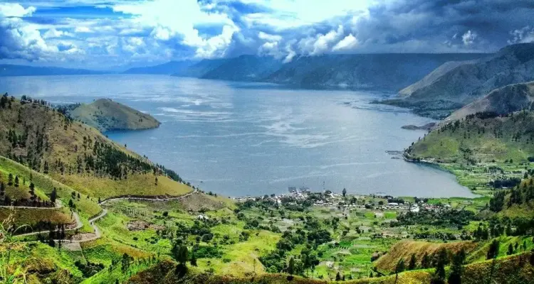 paket wisata danau toba: Panorama indah Danau Toba dari ketinggian dengan perbukitan hijau dan perkampungan di tepi danau, destinasi utama dalam paket wisata Danau Toba 3 hari 2 malam