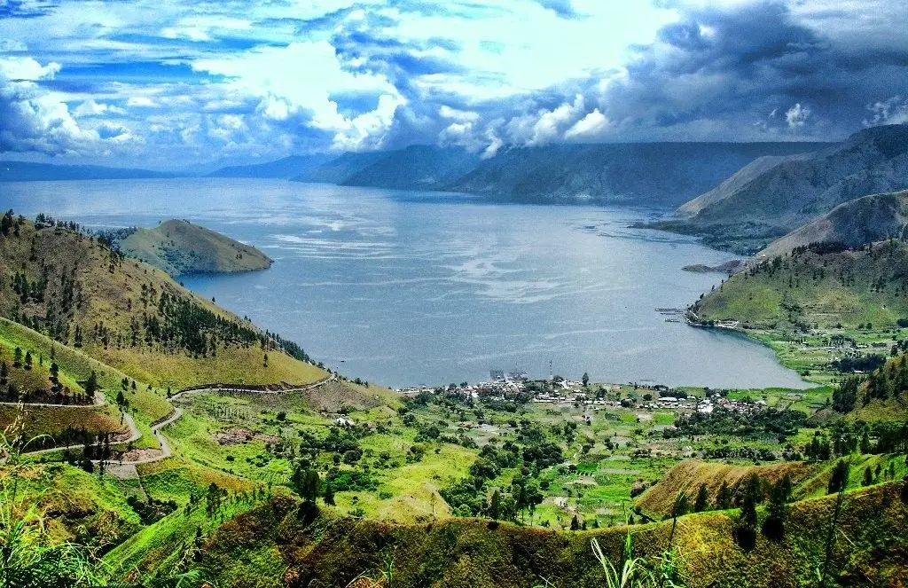 paket wisata danau toba: Panorama indah Danau Toba dari ketinggian dengan perbukitan hijau dan perkampungan di tepi danau, destinasi utama dalam paket wisata Danau Toba 3 hari 2 malam