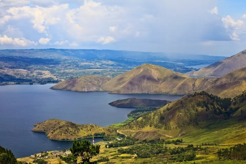 paket wisata danau toba: Pemandangan Danau Toba dengan perbukitan hijau dan pulau-pulau kecil di tengah danau, destinasi favorit untuk liburan keluarga dengan paket wisata yang praktis dan menyenangkan.