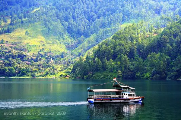 paket wisata danau toba: Perahu wisata di Danau Toba dengan latar perbukitan hijau.
